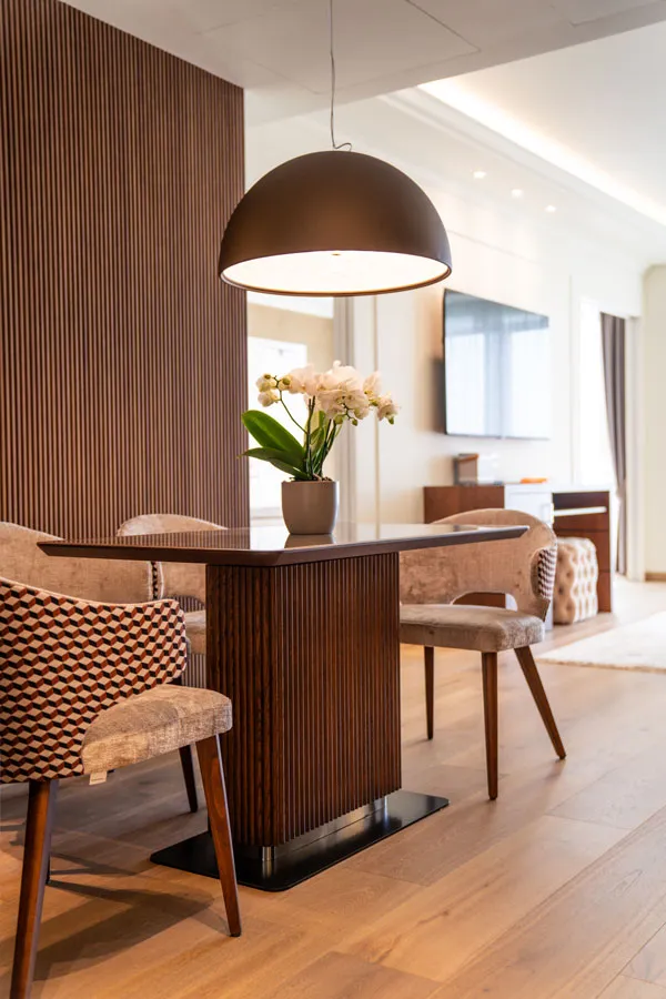 Classic contemporary hotel junior suite, square ceramic top table with fluted wooden legs and contemporary dining chairs in cream and pattern fabric