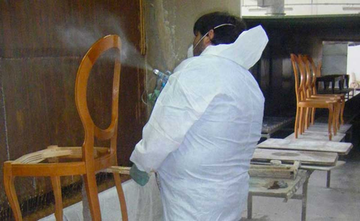 An operator polishing with a spray gun the structure of a classic wooden chair at Sevensedie in Italy