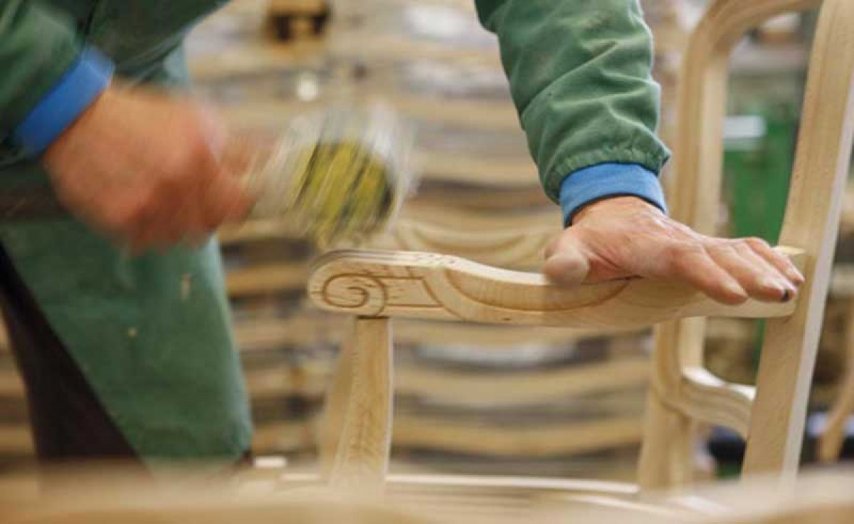 Operator assembling the armrest of a wooden chair at Sevensedie in Italy