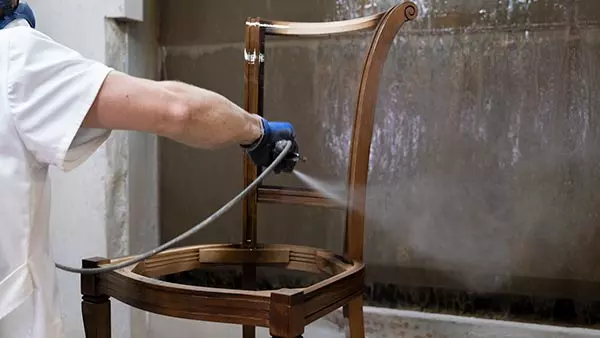 An operator polishing with a spray gun the structure of a classic wooden chair at Sevensedie in Italy