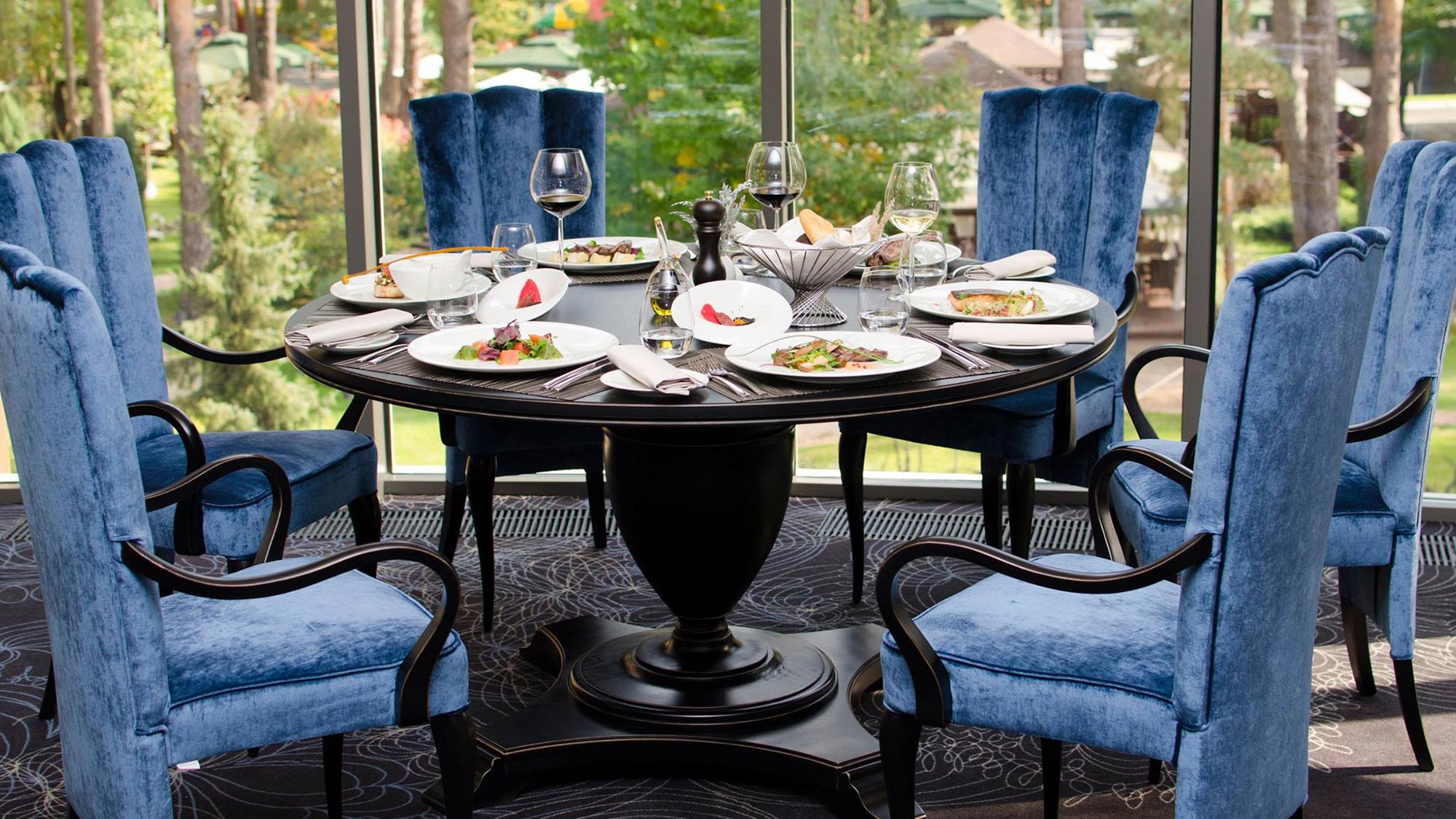 A large black lacquered classic round dining table Biscotus, surrounded by 6 hi back dining armchairs lacquered in black and upholstered in a crushed blue velvet