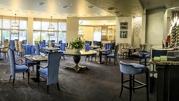 general view of the Mozart restaurant showing the full extension of the dining area. Contemporary Queen dining chairs with tufted back upholstered in gold velvet. Classic black lacquered high back armchairs together with a few square Atene dining tables an the Bisotus round table. On the right a couple of Arturo bar stools