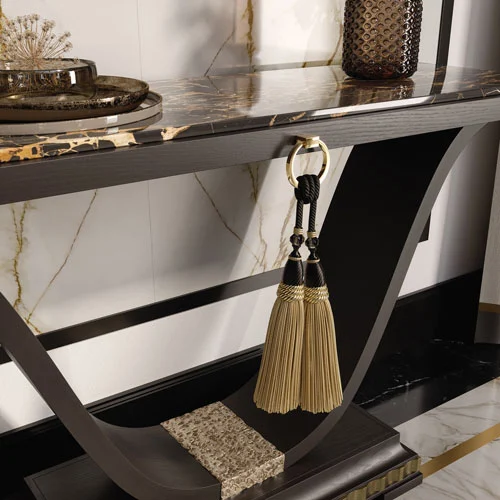 Una lussuosa consolle contemporanea laccata nero opaco, con dettagli in foglia d'oro anticata, nappe decorative in tessuto e piano in marmo Portoro